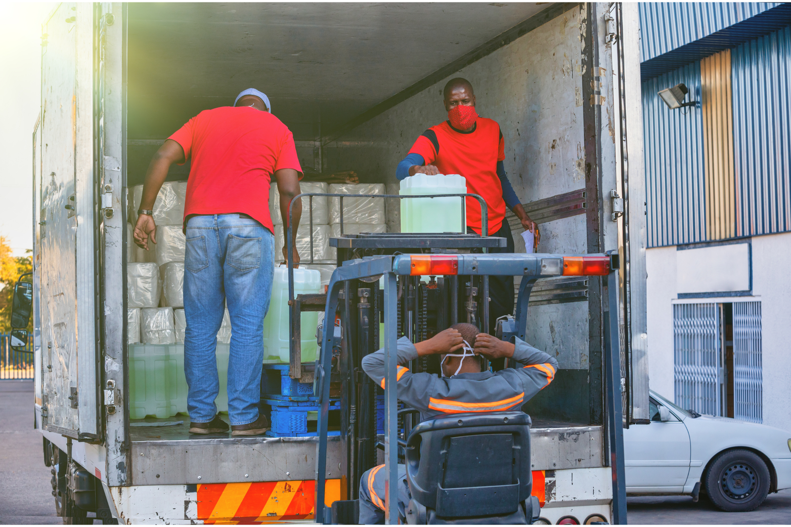 Workers using a forklift to load palletized goods and containers into a truck for a full container load shipment